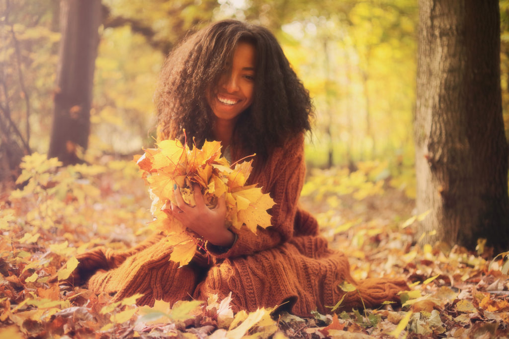 young black girl sitting in the leaves in the fall. 
